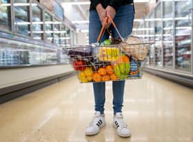 A woman holds a basket of goods in a supermarket.