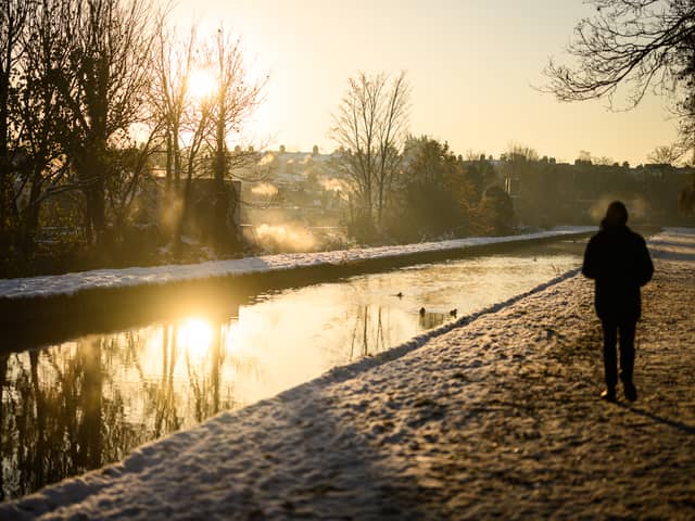 A man walks on the snow-covered path by the New River at sunrise, as steam rises from nearby houses in London.