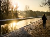 A man walks on the snow-covered path by the New River at sunrise, as steam rises from nearby houses in London.