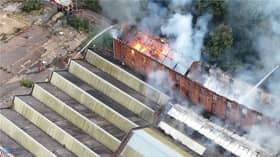 Flames and smoke pour from roof of factory building.