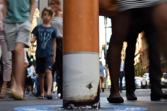 Shoppers walk past a bollard painted to represent a cigarette butt to raise awareness about 'smoke free' zones. Picture: SAEED KHAN/AFP via Getty Images.
