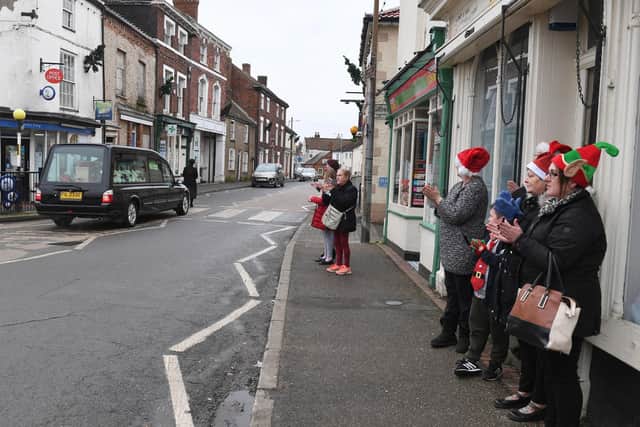 Members of the community clap as the funeral procession passes by.
