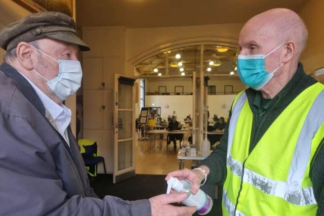 Patient Melvyn Sherlock gets a shot of hand sanitiser from volunteer Malcolm Fielder on arrival at the Franklin Hall in Spilsby.