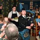 Addressing the Haggis is John Mackenzie.  Kirsteen Macdonald of RAF Waddington pipes and drums, and apprentice chef Blue Charles carrying the haggis. EMN-220126-102619001