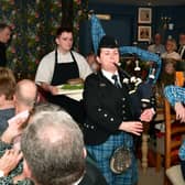 Addressing the Haggis is John Mackenzie.  Kirsteen Macdonald of RAF Waddington pipes and drums, and apprentice chef Blue Charles carrying the haggis. EMN-220126-102619001