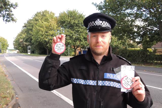 Neighbourhood Policing Sergant Stuart Mumby-Croft, covering Sleaford and its surrounding rural areas, displaying some of the new campaign air fresheners reminding motorists to "Belt up. Hang up. Ease up." EMN-210929-150338001