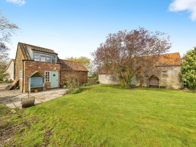 To the rear of the annexe, with barns behind the tree.