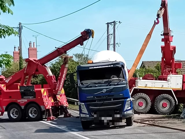Recovery trucks winch the cement mixer back onto its wheels.