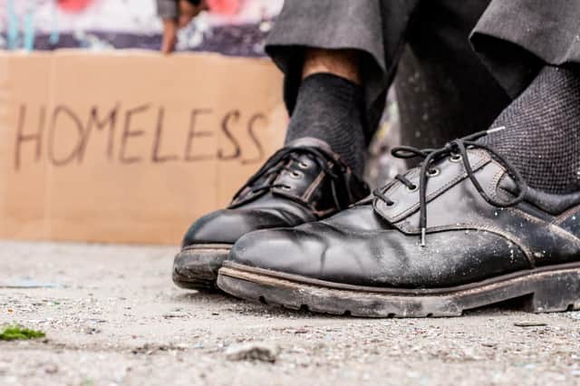 Homeless man sitting on the street near the sign. Photo: Getty Images/iStockphoto