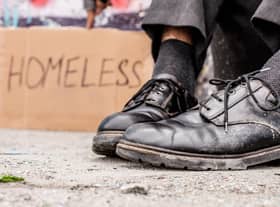 Homeless man sitting on the street near the sign. Photo: Getty Images/iStockphoto