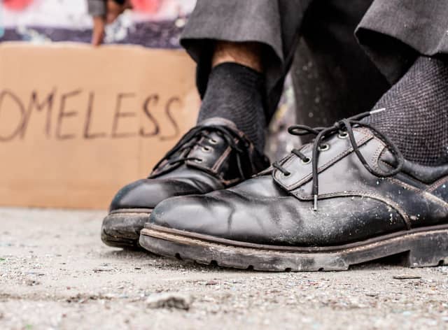 Homeless man sitting on the street near the sign. Photo: Getty Images/iStockphoto