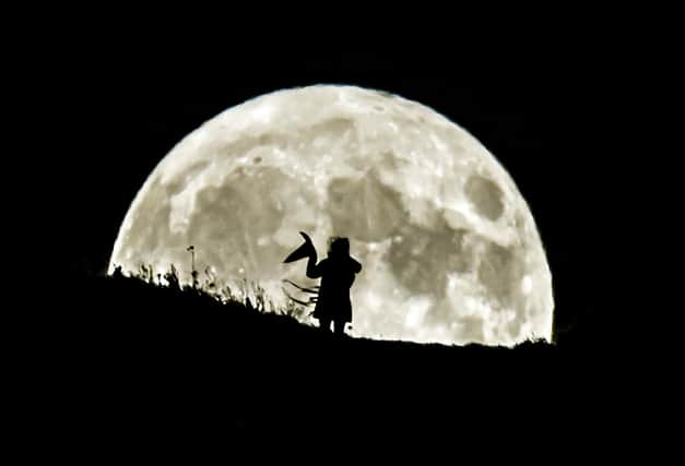 A person holding a witch's hat watches the Blue Moon rise over Castle Hill in Huddersfield, it will be the last full moon to fall on Halloween until 2039.