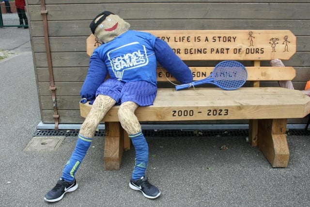 A tennis  player scarecrow takes a rest on a bench