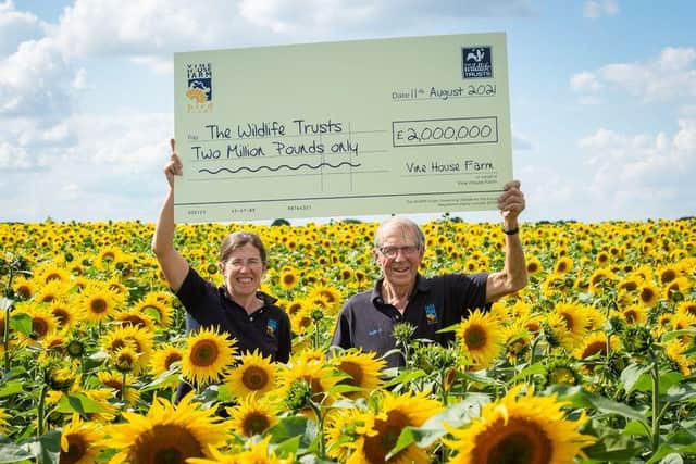 Lucy Taylor, manager and Nicholas Watts, farmer, holding cheque for £2 million in sunflower field