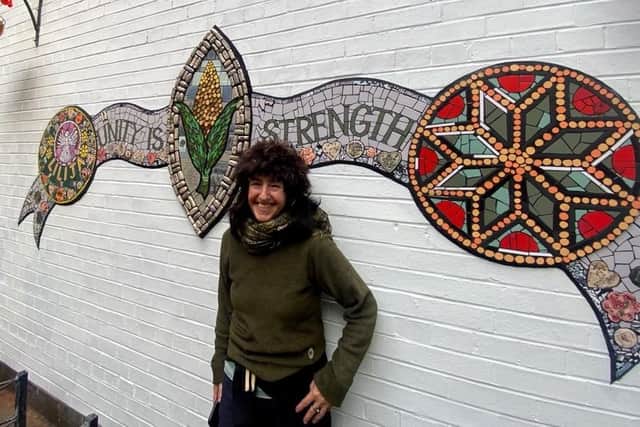 Lead artist Karen Francesca stands in front of the crest mosaic artwork.