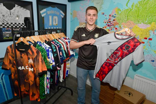 Louis Jones wearing a Jamaica away short, holding a shirt of Uprising FC in Anguilla, sponsored by Surprise Shirt.