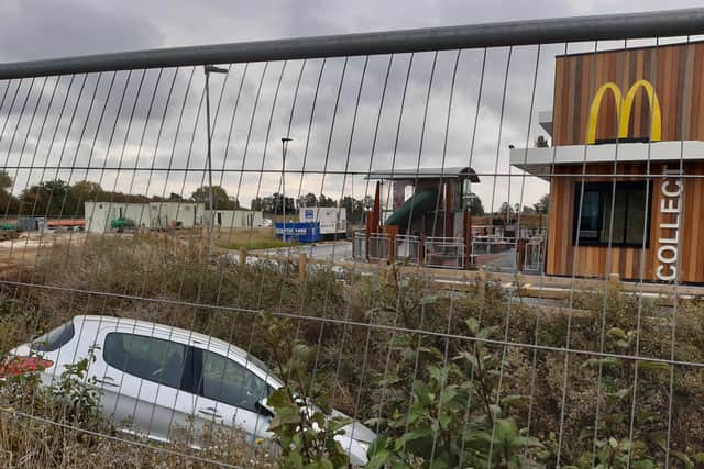 Despite progress with the scheme, the car lying in the ditch that runs next to the new McDonald's remains in place behind the fencing.