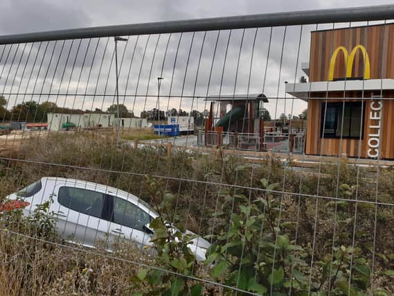 Despite progress with the scheme, the car lying in the ditch that runs next to the new McDonald's remains in place behind the fencing.