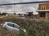 Despite progress with the scheme, the car lying in the ditch that runs next to the new McDonald's remains in place behind the fencing.