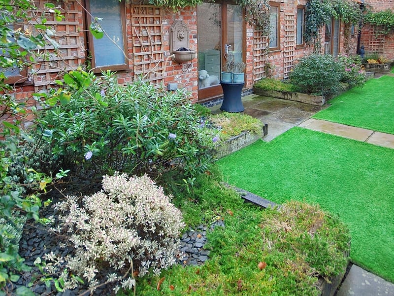 The artificial lawn is surrounded by well-stocked flower and shrubbery borders.