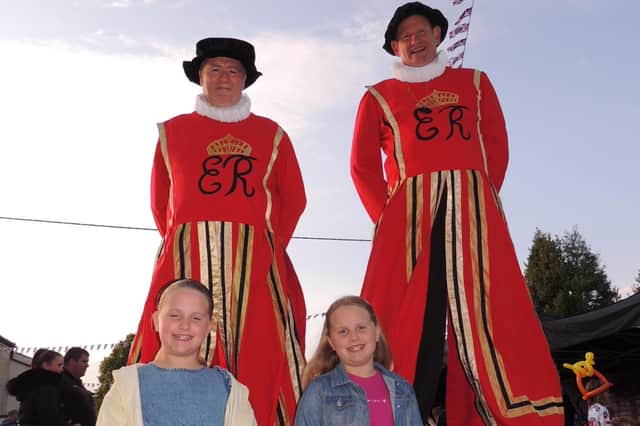 Fun at Metheringham's beacon lighting event. Eight year-old twins Bella and Olivia Pearson from the village with stiltwalking 'beefeaters'.