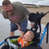 Joey laughing as he is able to go in the sea for the first time, watched by dad Tom.
