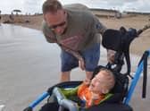 Joey laughing as he is able to go in the sea for the first time, watched by dad Tom.