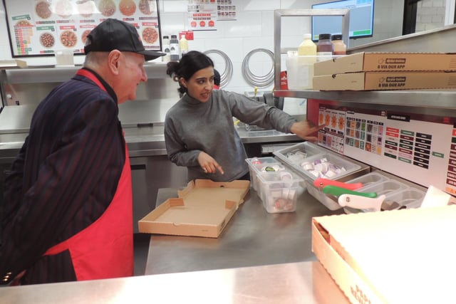 Simran Bains explains the art of evenly slicing pizza to Mayor Anthony Brand.
