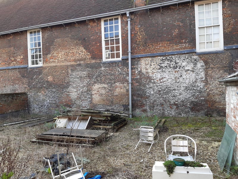 To the rear of the building is an open area that borders The Guildhall. It is laid with thick slabs of stone, estimated to be hundreds of years old. This picture looks towards The Guildhall and appears to show the outline of buildings that once stood against it. The area is also home to a large freshwater cistern, hidden beneath a slab of stone, and a former sugar boiler workshop.