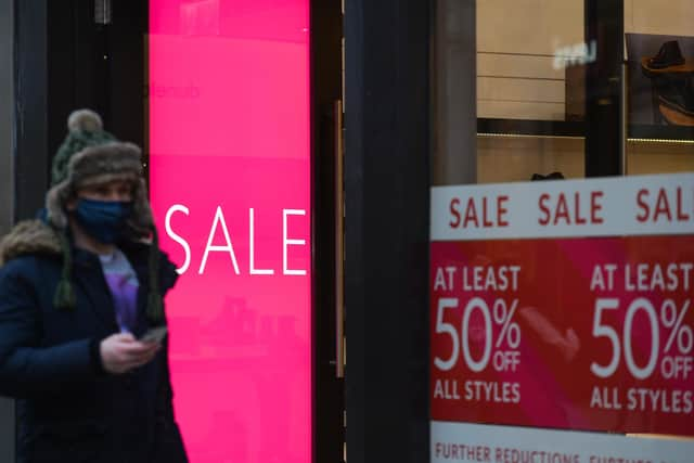 A man wearing a face mask walks past signs advertising sales. (Photo by Artur Widak/NurPhoto via Getty Images)