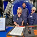 Mairi Perry, fundraising chairman, signs the RNLI 200 scroll at Skegness Lifeboat Station, watched by Coxwain Craig Willard and volunteer shop manager Chris Fisher.