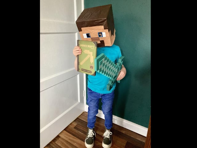 Finley Seymour, five, of Boston, as Steve from Minecraft, with one of his favourite books - Minecraft: Beginner's Handbook.