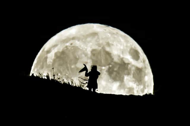 A person holding a witch's hat watches the Blue Moon rise over Castle Hill in Huddersfield, it will be the last full moon to fall on Halloween until 2039.