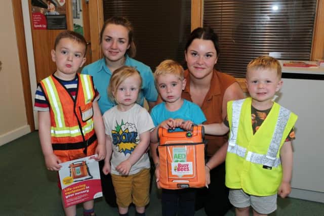 Children from the early years hold the defibrillator with teacher Nikki Skyes and manager Emily Atkins.