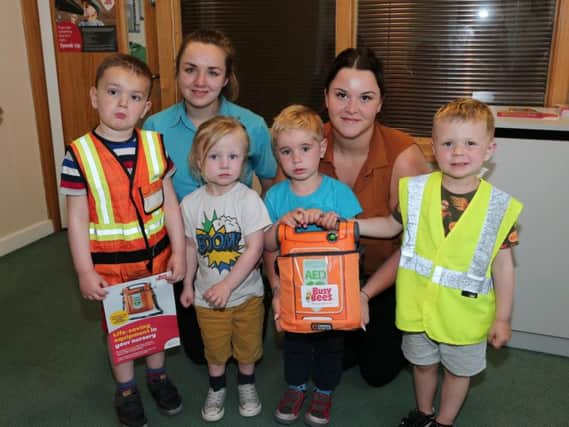 Children from the early years hold the defibrillator with teacher Nikki Skyes and manager Emily Atkins.