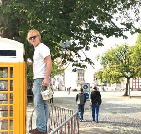 John Byford in Bad Gandersheim market sqaure painting the telephone white as a symbol of peace. ANL-180211-111331001