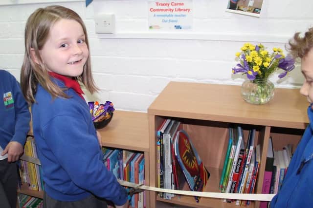 A pupil cuts the ribbon to open the library. The plaque in memory of Mrs Carne can be seen on the wall above.
