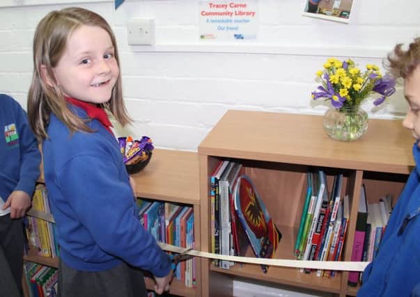 A pupil cuts the ribbon to open the library. The plaque in memory of Mrs Carne can be seen on the wall above.