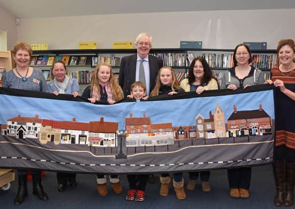 Pictured holding a tapestry of the shops in Wragby Market Place are children, mums and organisers of the recently opened Wragby Community Hub - Barbara Barlett, Maureen Thompson, Amy and Lucy Lowman, Mathew Bacon, Coun Nick Guyatt, Vivien Lewis, Dani Bacon and Clare Lee. Photo by John Edwards EMN-160223-151132001