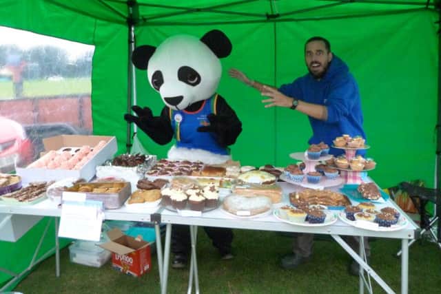 Caistor Running Club cake stall, manned by Chris Ramsay, being 'attacked' by Robey the Panda (Jayne McConochie). EMN-160921-170452001