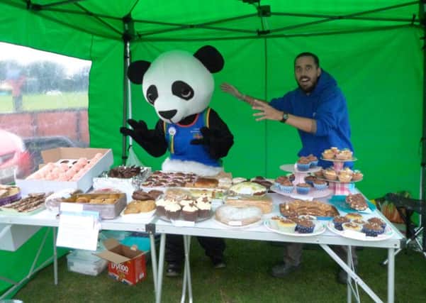 Caistor Running Club cake stall, manned by Chris Ramsay, being 'attacked' by Robey the Panda (Jayne McConochie). EMN-160921-170452001