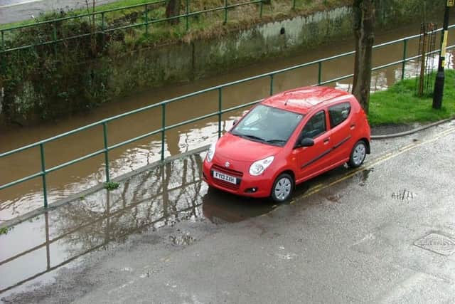 A car parked in a flooded parking bay with the River Waring behind