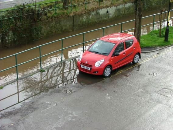 A car parked in a flooded parking bay with the River Waring behind